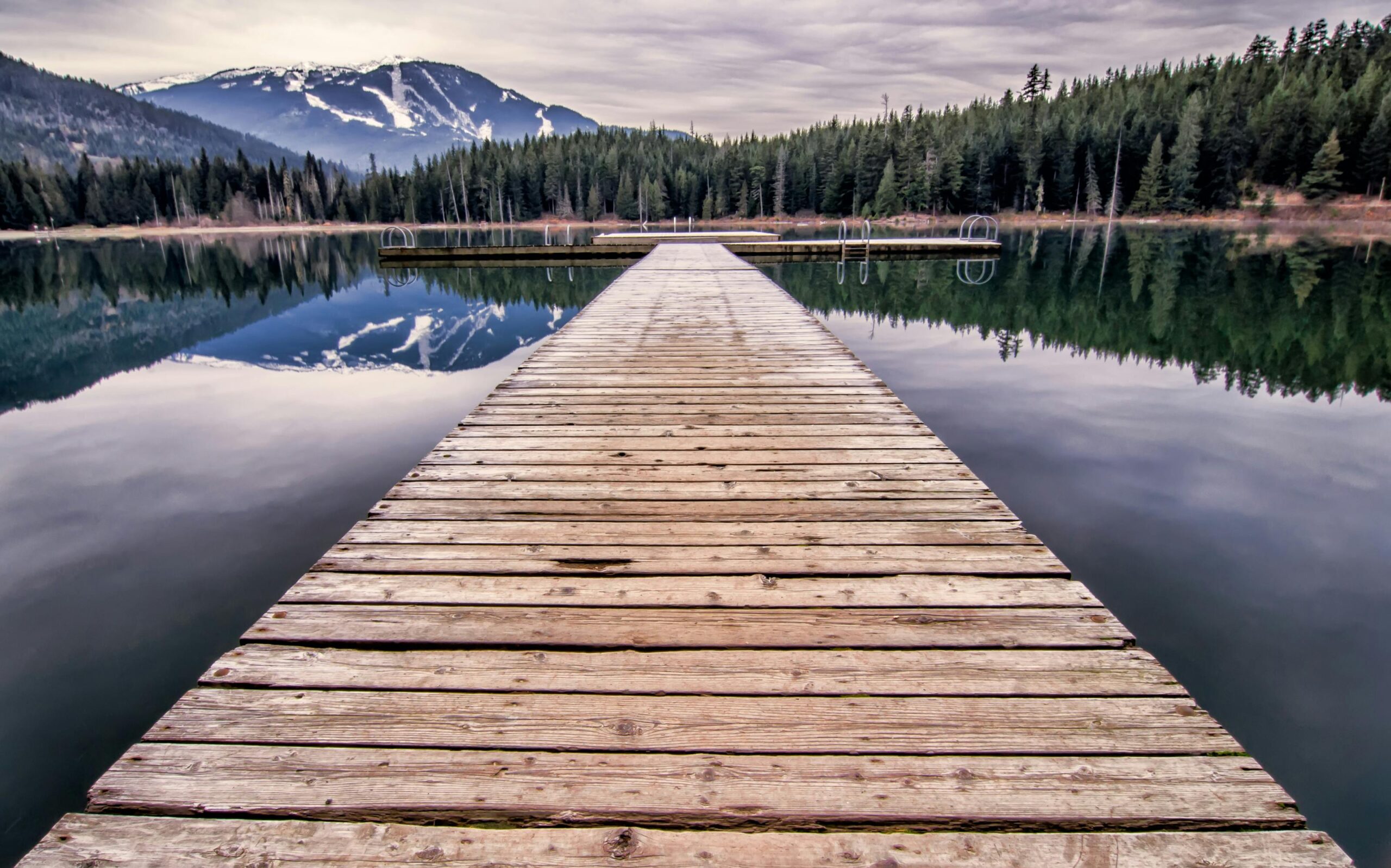 A peaceful view of a wooden dock leading to a mountain lake in Whistler, BC, Canada.